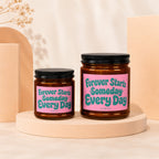 Two amber glass candles with pink labels reading "Forever Starts Someday Every Day".