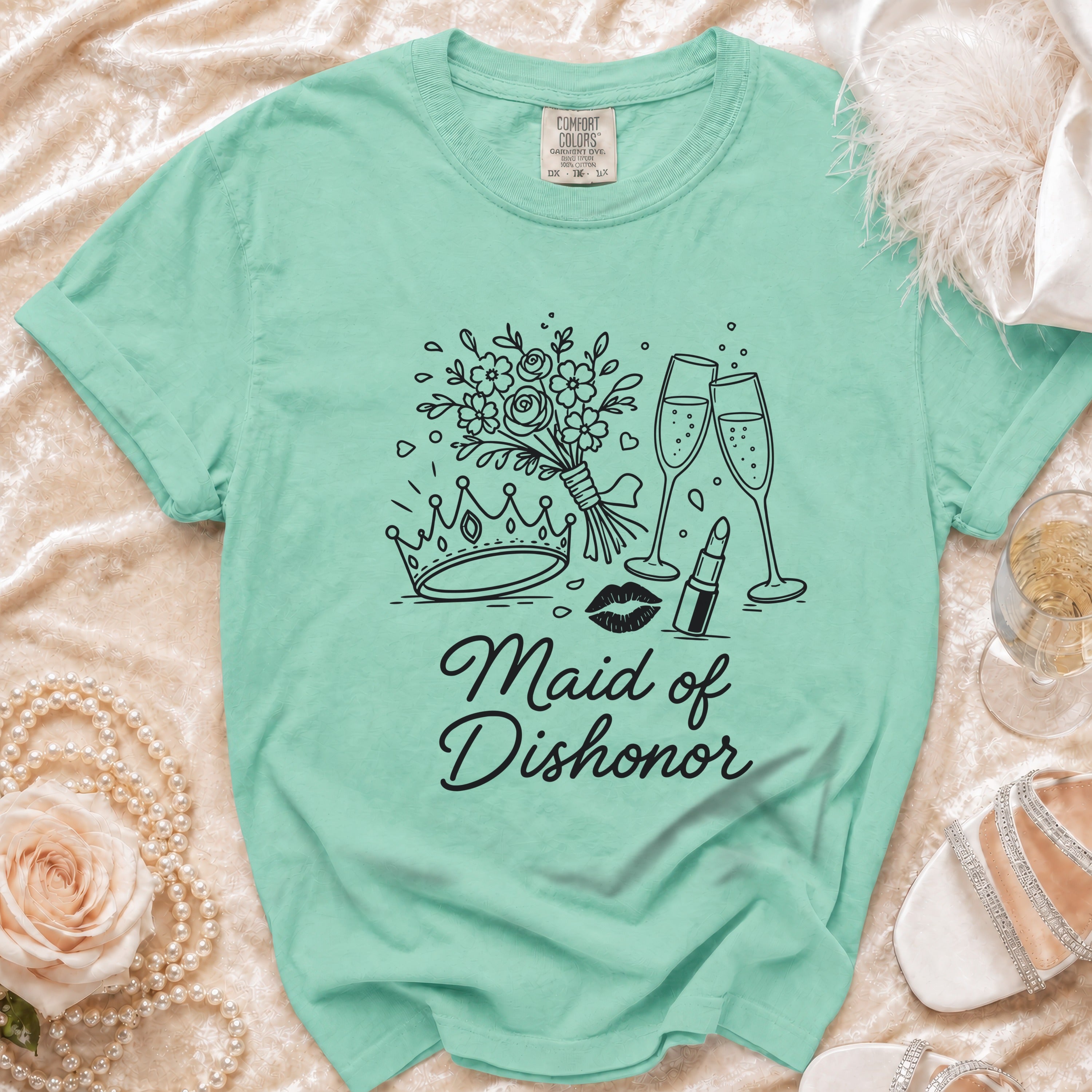 Mint green t-shirt with black line art of crown, flowers, champagne glasses, lipstick, and lips. Text reads "Maid of Dishonor."