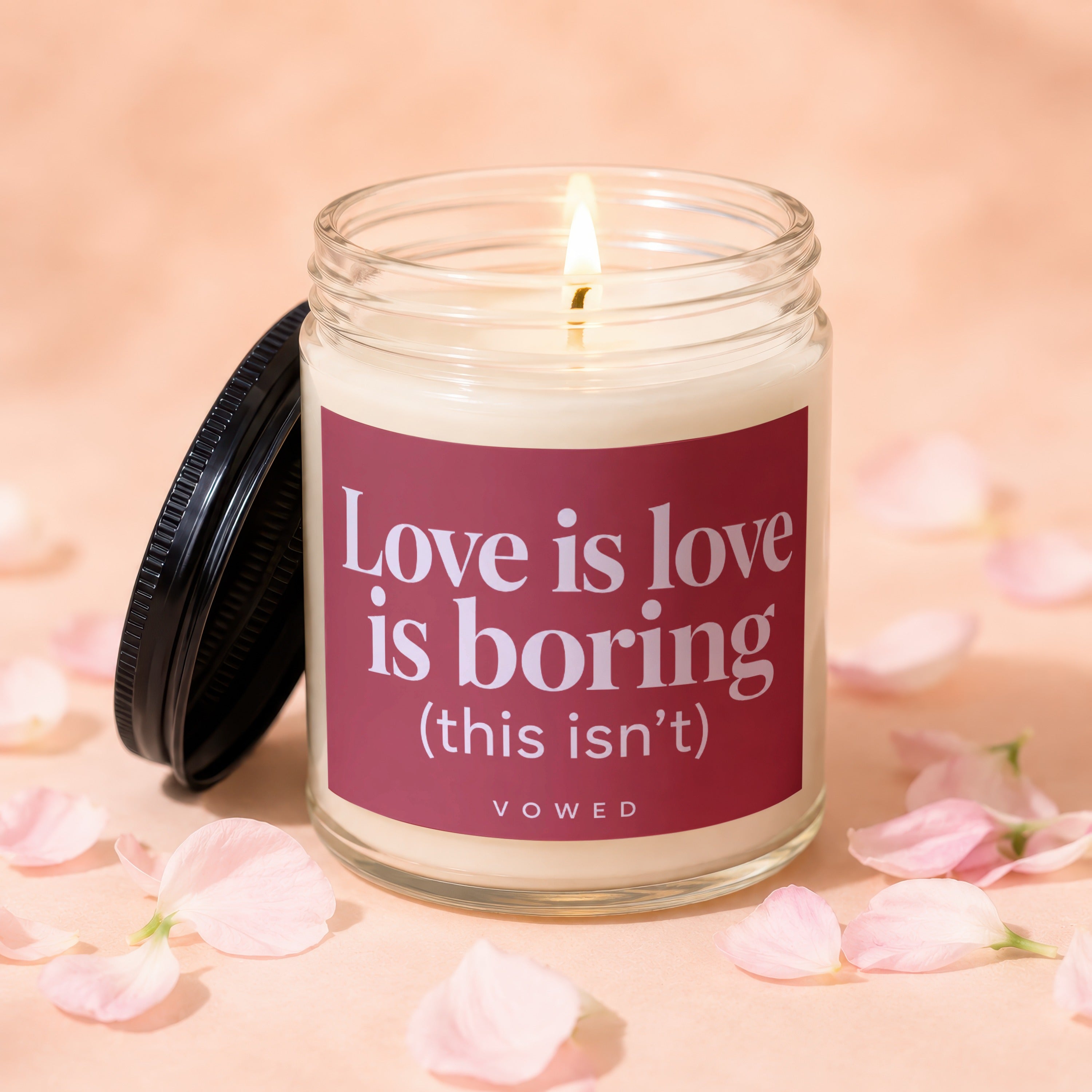 Candle with text "Love is love is boring (this isn't)" on pink background.