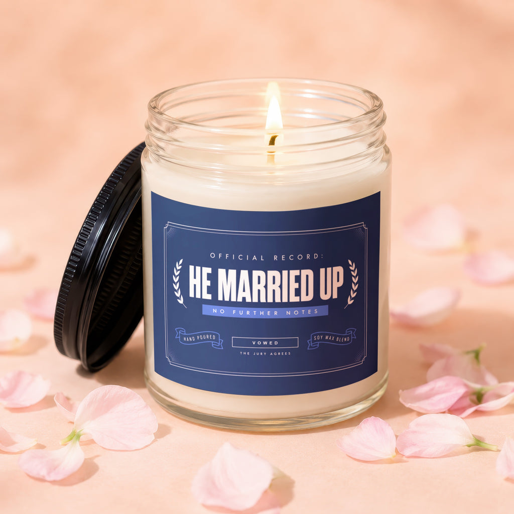 Lit candle with "He Married Up" text, soy wax blend, hand-poured, vowed.