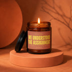 Amber jar candle with lid off, lit, reading "We understood the assignment"