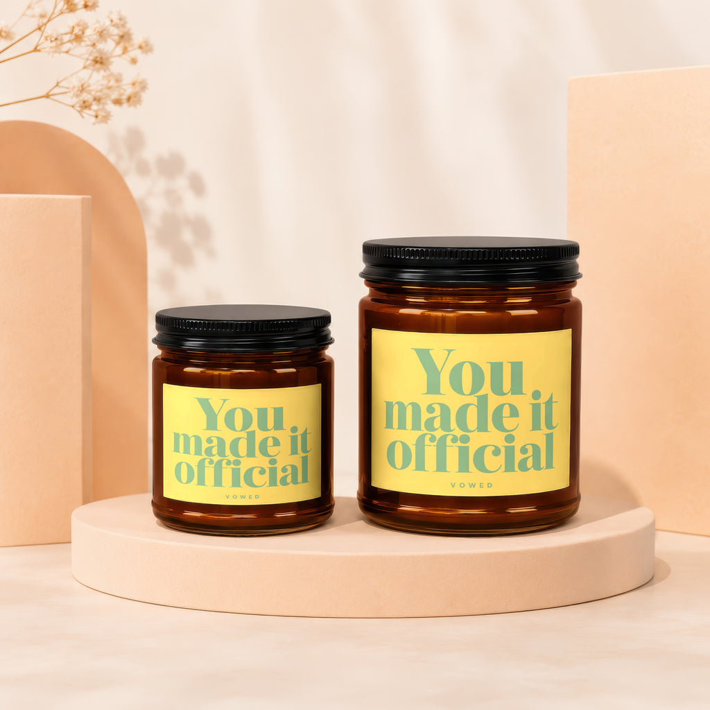 Two amber glass candles with yellow labels reading "You. made it official" by Vowed.