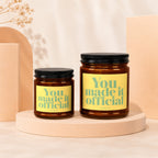 Two amber glass candles with yellow labels reading "You. made it official" by Vowed.