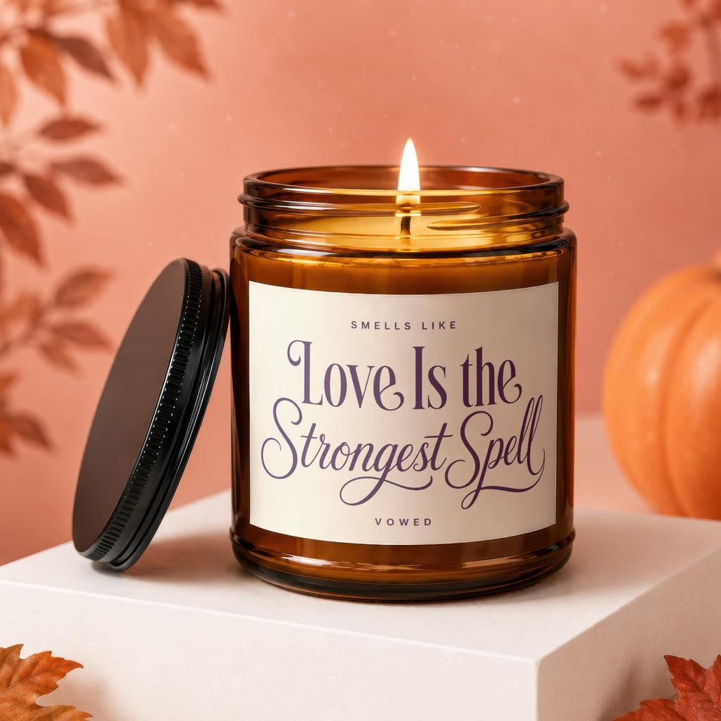 Amber jar candle with lit wick reads "Love Is the Strongest Spell"