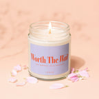 Lit candle in a glass jar with "Worth The Wait" and "Vowed" text, surrounded by petals.