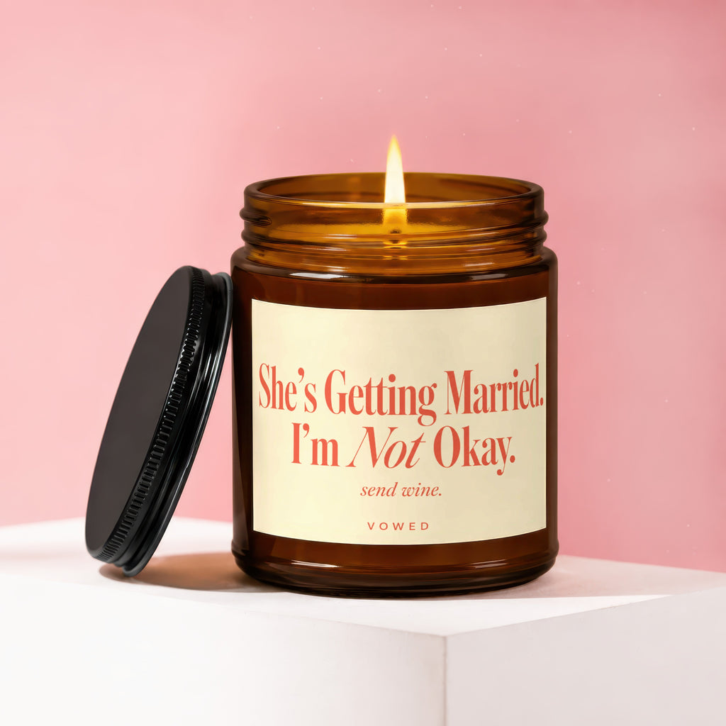 Amber jar candle with lit wick and black lid, text reads "She's Getting Married. I'm Not Okay. send wine."