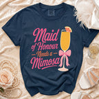 Navy t-shirt with "Maid of Honour Needs a Mimosa" graphic and mimosa cocktail.