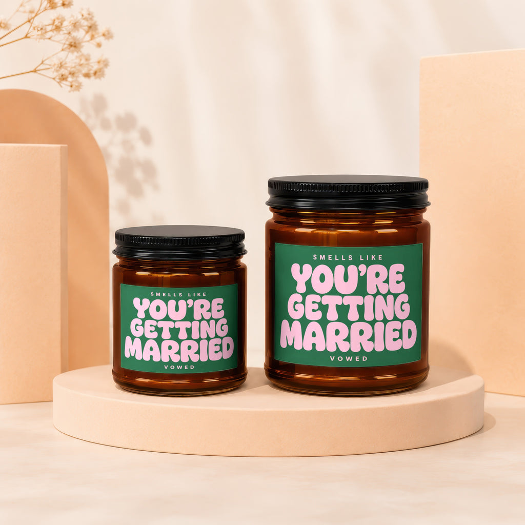 Two amber glass candles with green labels that say "Smells Like You're Getting Married".