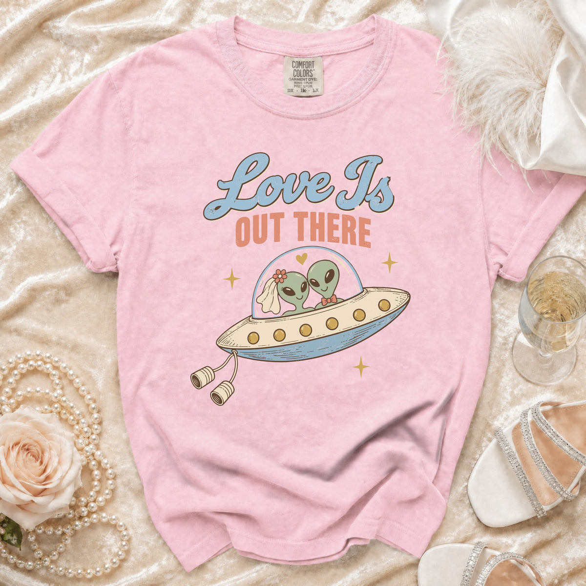 Pink t-shirt with graphic of two aliens in a UFO, reading "Love Is OUT THERE".