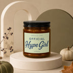 Amber candle labeled "Smells Like Official Hype Girl" on a pedestal with pumpkins.