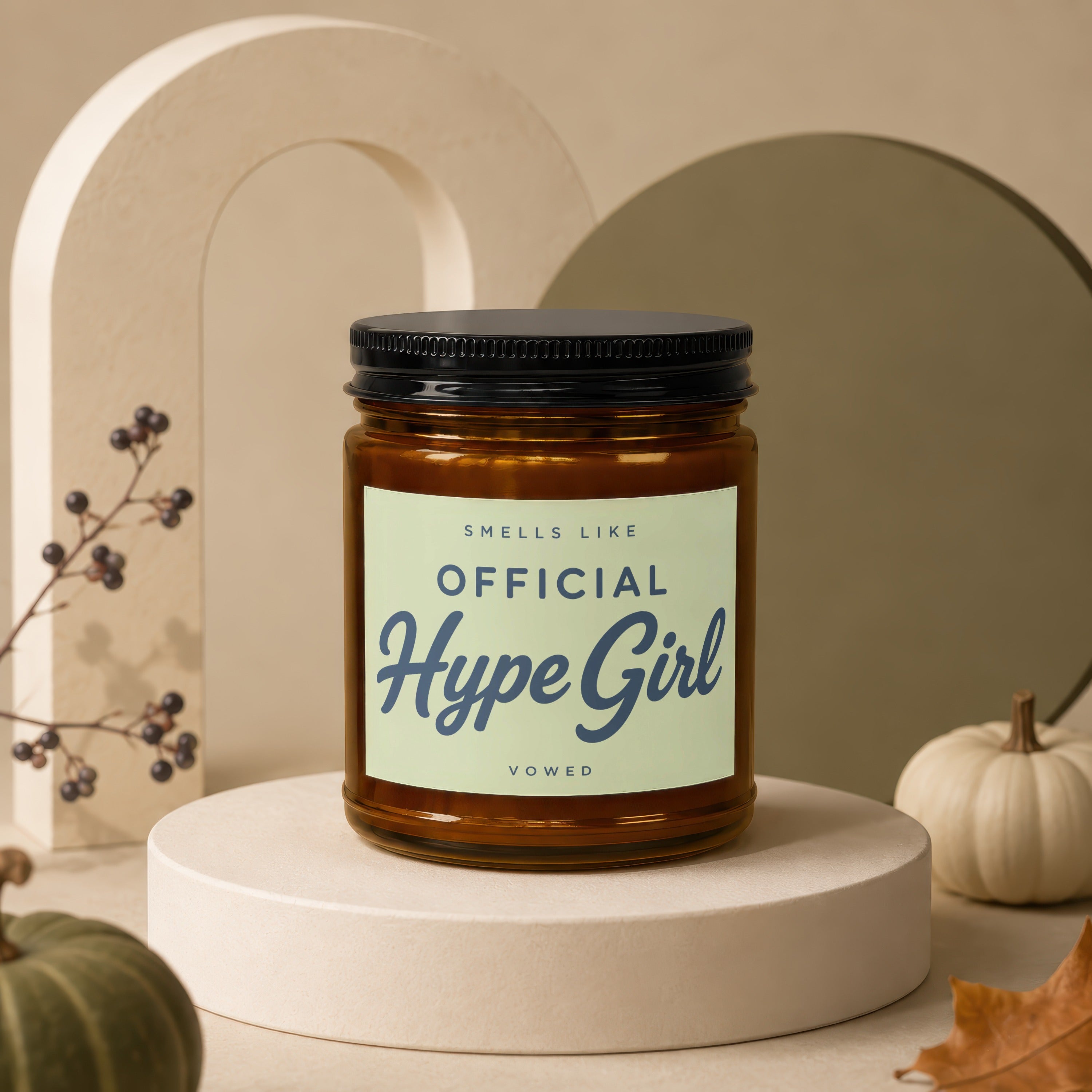 Amber candle labeled "Smells Like Official Hype Girl" on a pedestal with pumpkins.
