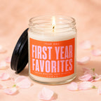 Glass candle with orange label reading "First Year Favorites" with pink text.