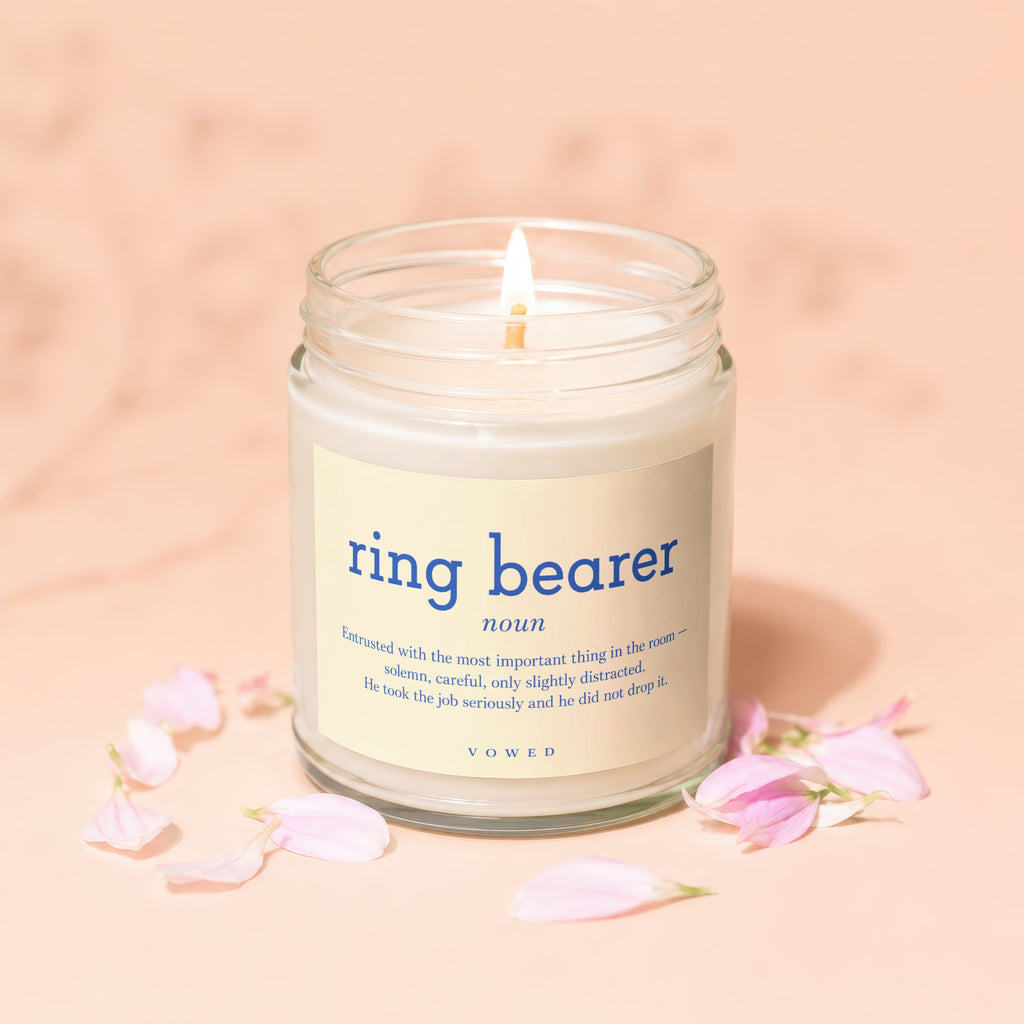 Jar candle with "ring bearer" definition and VOWED branding surrounded by pink petals.