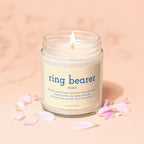 Jar candle with "ring bearer" definition and VOWED branding surrounded by pink petals.
