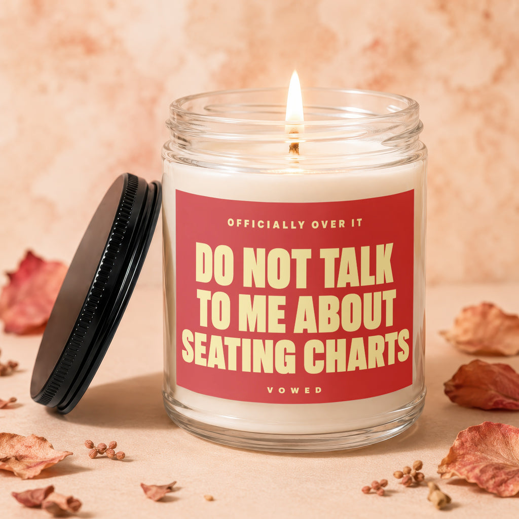 Glass candle with lit wick and red label reading "DO NOT TALK TO ME ABOUT SEATING CHARTS".