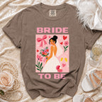 Bride To Be graphic on a t-shirt with a bride, flowers, and champagne.
