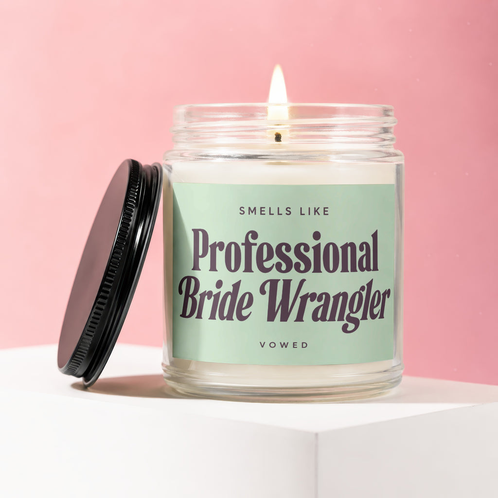 Lit candle with "Smells Like Professional Bride Wrangler Vowed" text on a pale green label.