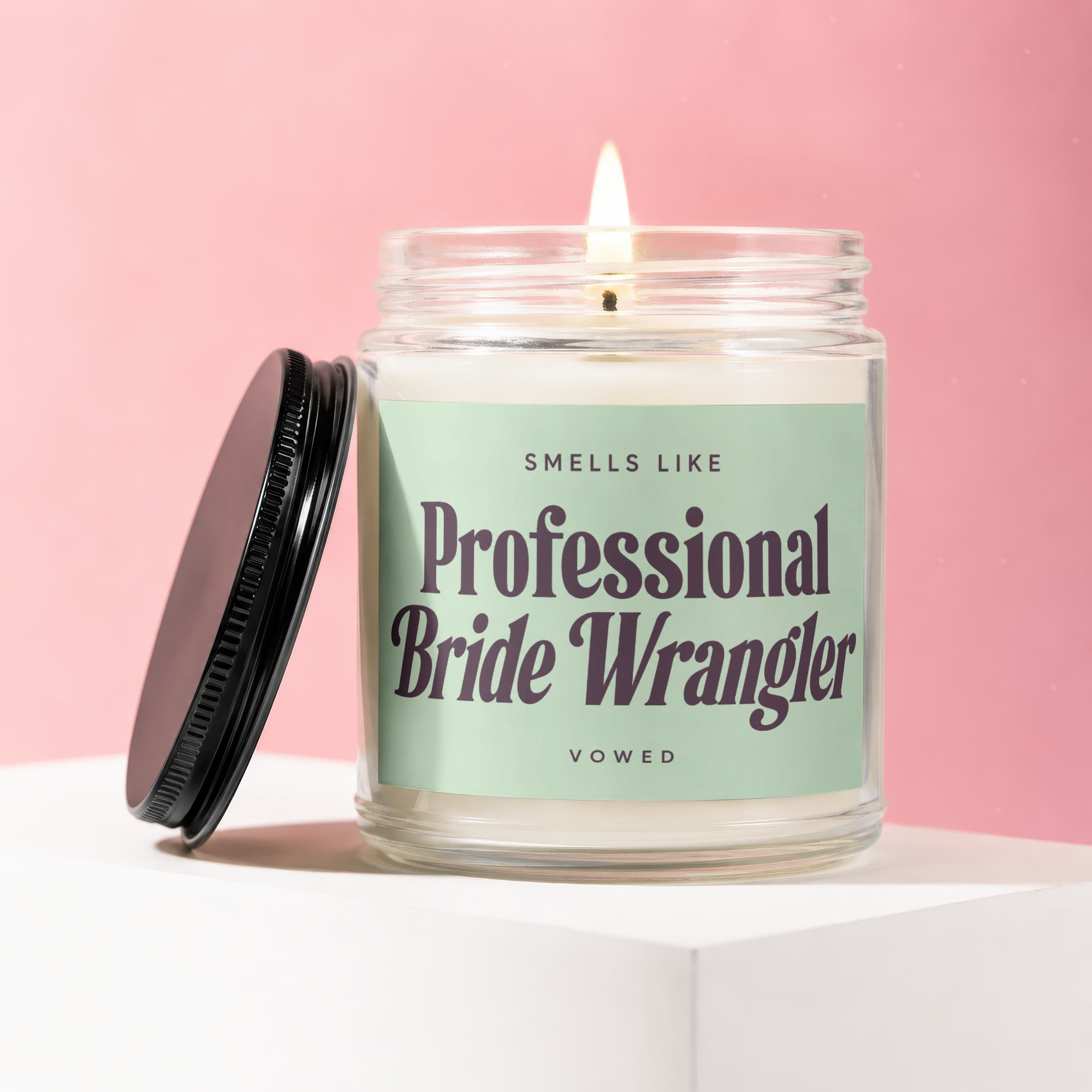 Lit candle with "Smells Like Professional Bride Wrangler Vowed" text on a pale green label.