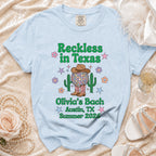 Light blue t-shirt with "Reckless in Texas" and "Olivia's Bach Austin, TX Summer 2026" text.