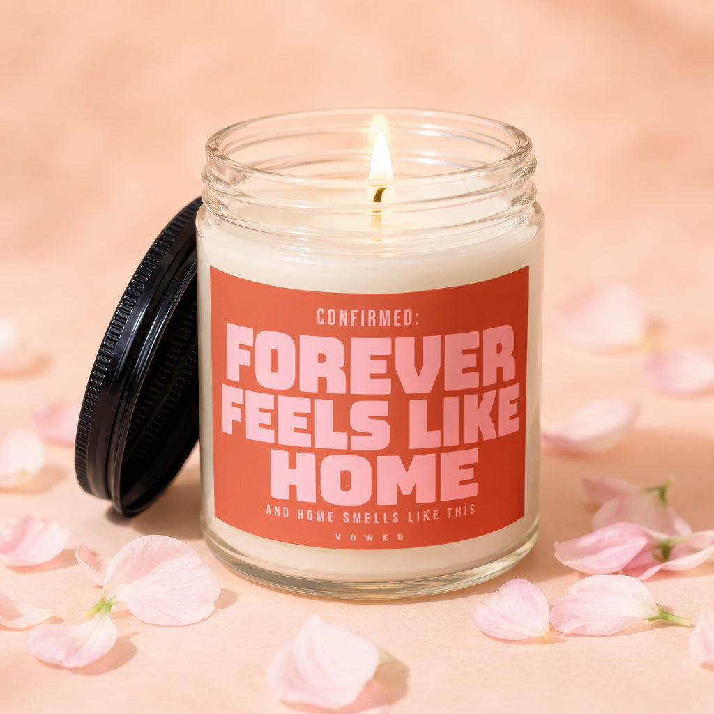 Glass candle with pink label stating "Forever Feels Like Home" and a lit wick.