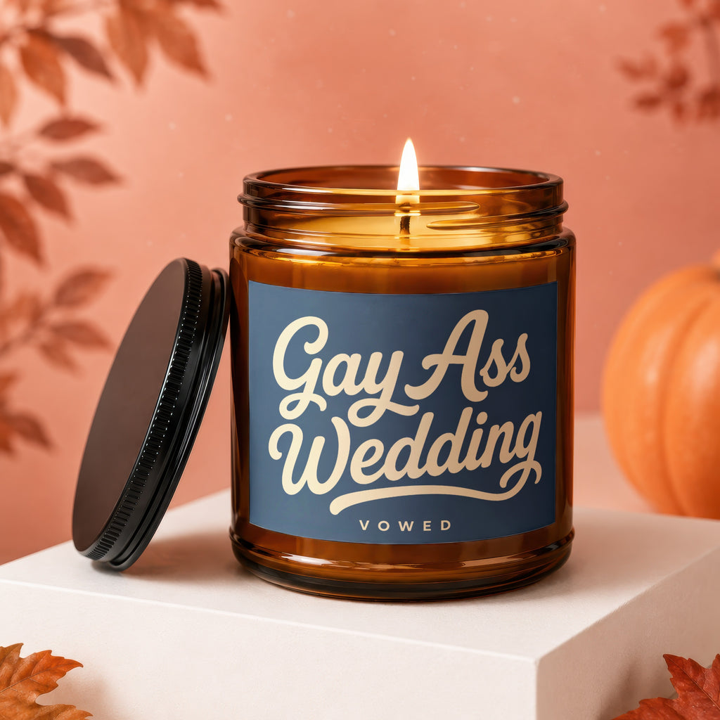 Amber jar candle with lit flame, reads "Gay Ass Wedding" on dark blue label.