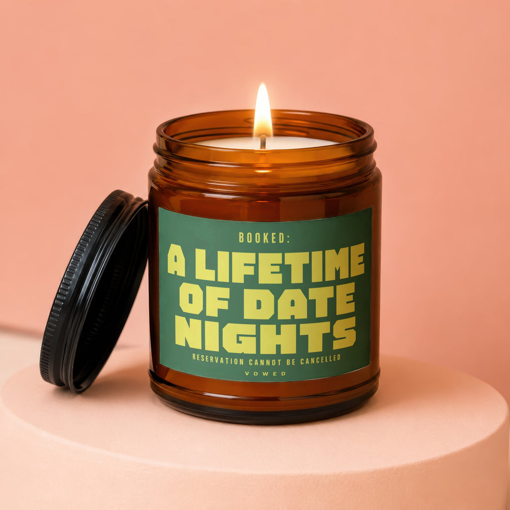 Amber jar candle with lit wick and lid, reads "Booked: A Lifetime of Date Nights."