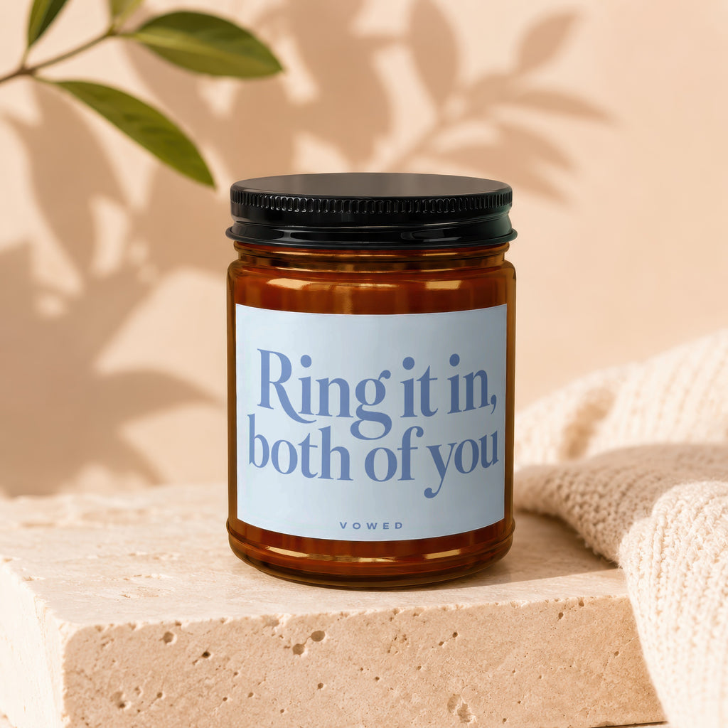 Amber jar candle with light blue label reading "Ring it in, both of you" and "vowed".