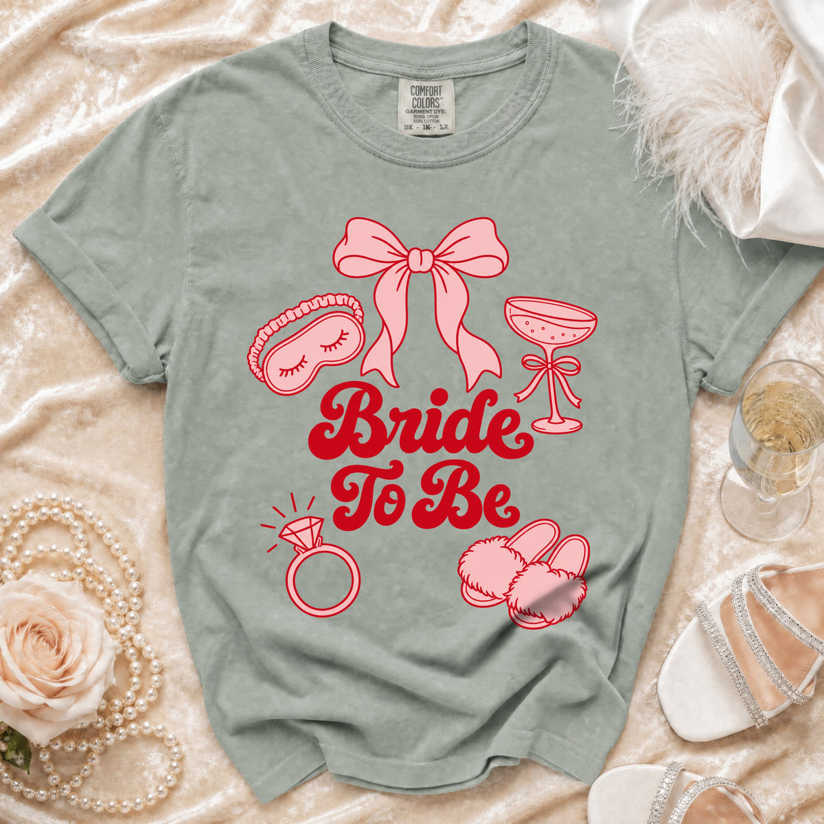 Sage green t-shirt with "Bride To Be" text and bridal icons in pink.