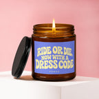 Amber glass candle lit, with a blue label reading "RIDE OR DIE, NOW WITH A DRESS CODE."