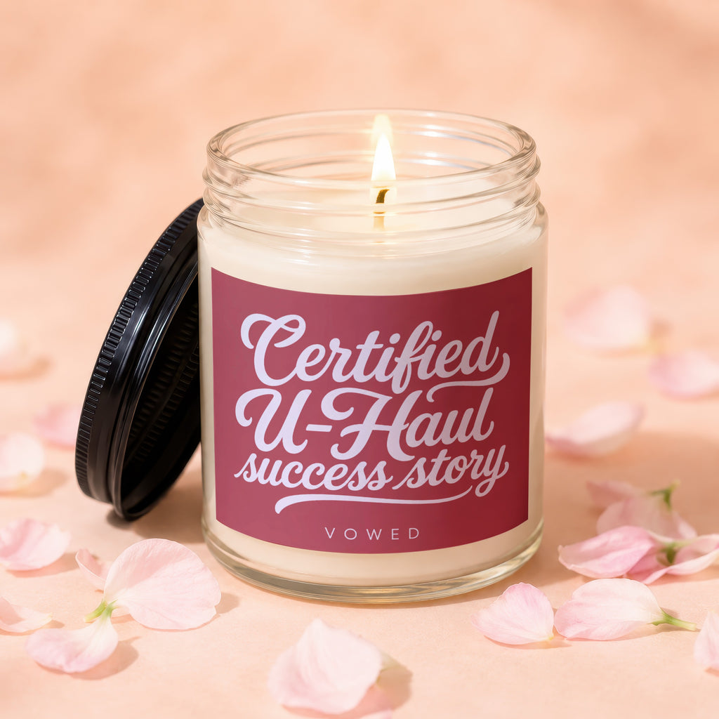 Jar candle with a lit wick and a maroon label that reads "Certified U-Haul success story VOWED."