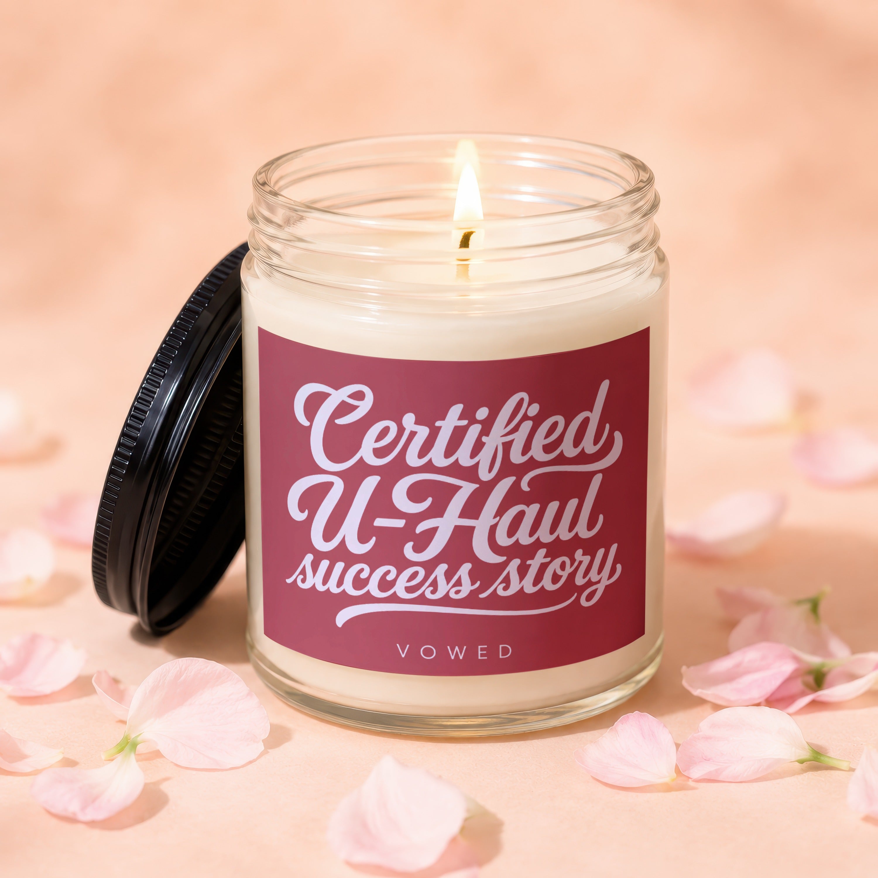 Jar candle with a lit wick and a maroon label that reads "Certified U-Haul success story VOWED."