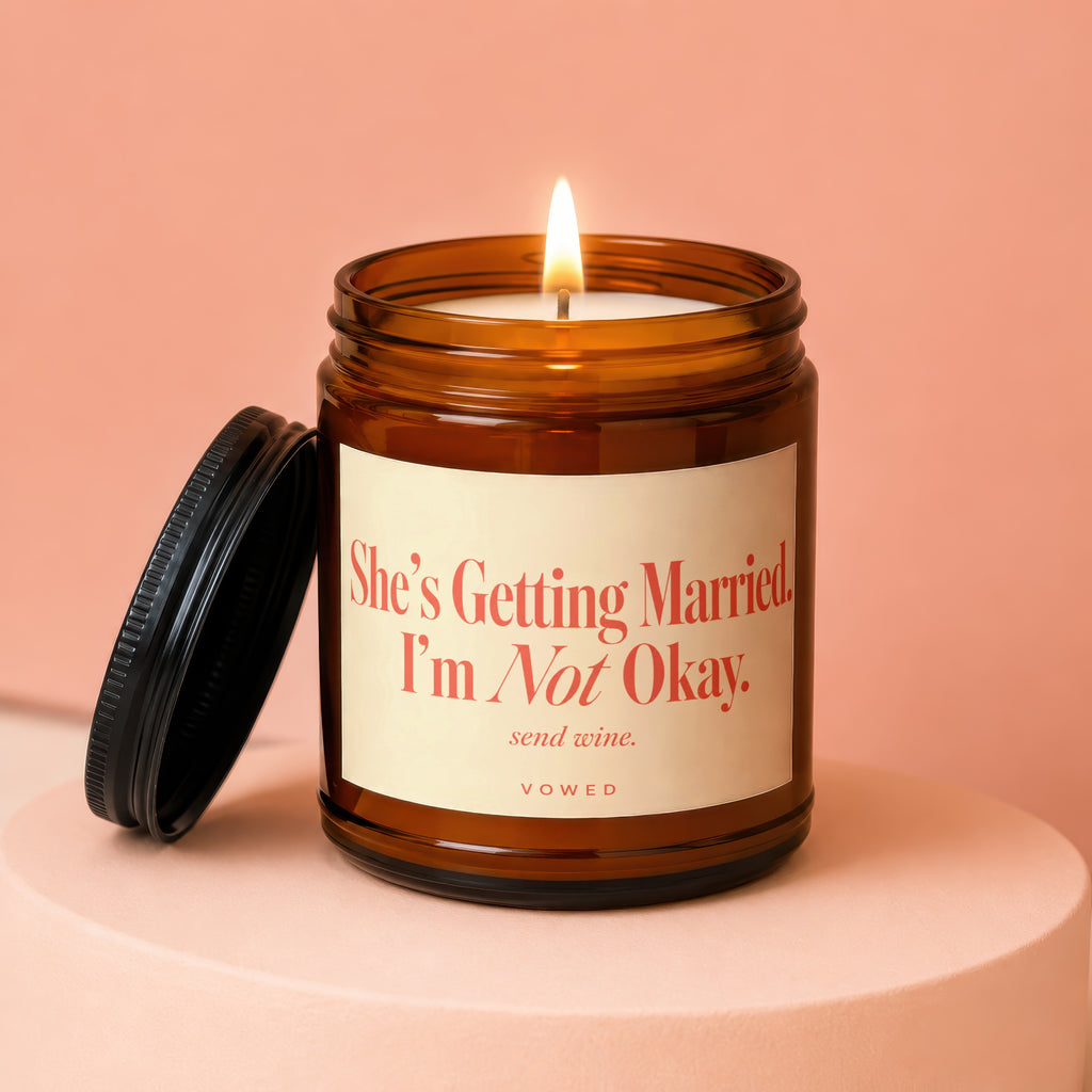 Amber jar candle with lit flame and label stating "She's Getting Married. I'm Not Okay. send wine."