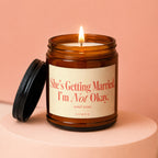 Amber jar candle with lit flame and label stating "She's Getting Married. I'm Not Okay. send wine."