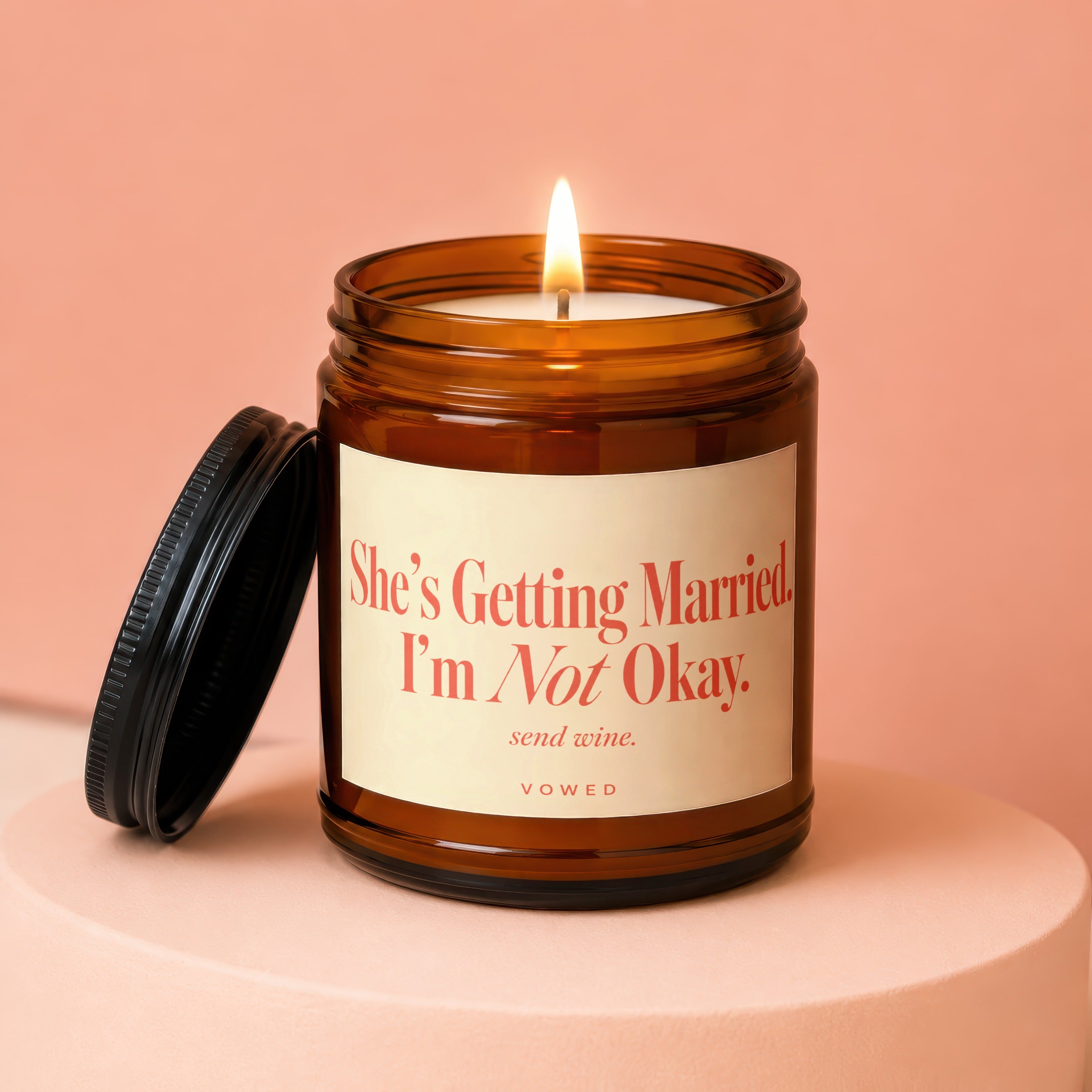 Amber jar candle with lit flame and label stating "She's Getting Married. I'm Not Okay. send wine."