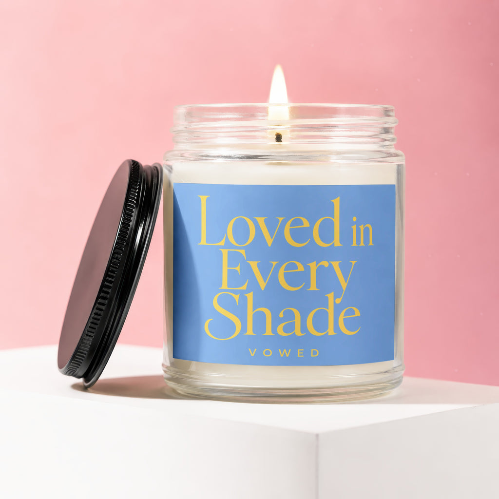 Candle with lit wick and blue label reading "Loved in Every Shade VOWED".