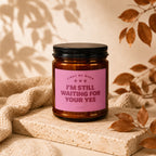 Brown glass candle with pink label reading "Light Me When I'm Still Waiting For Your Yes."