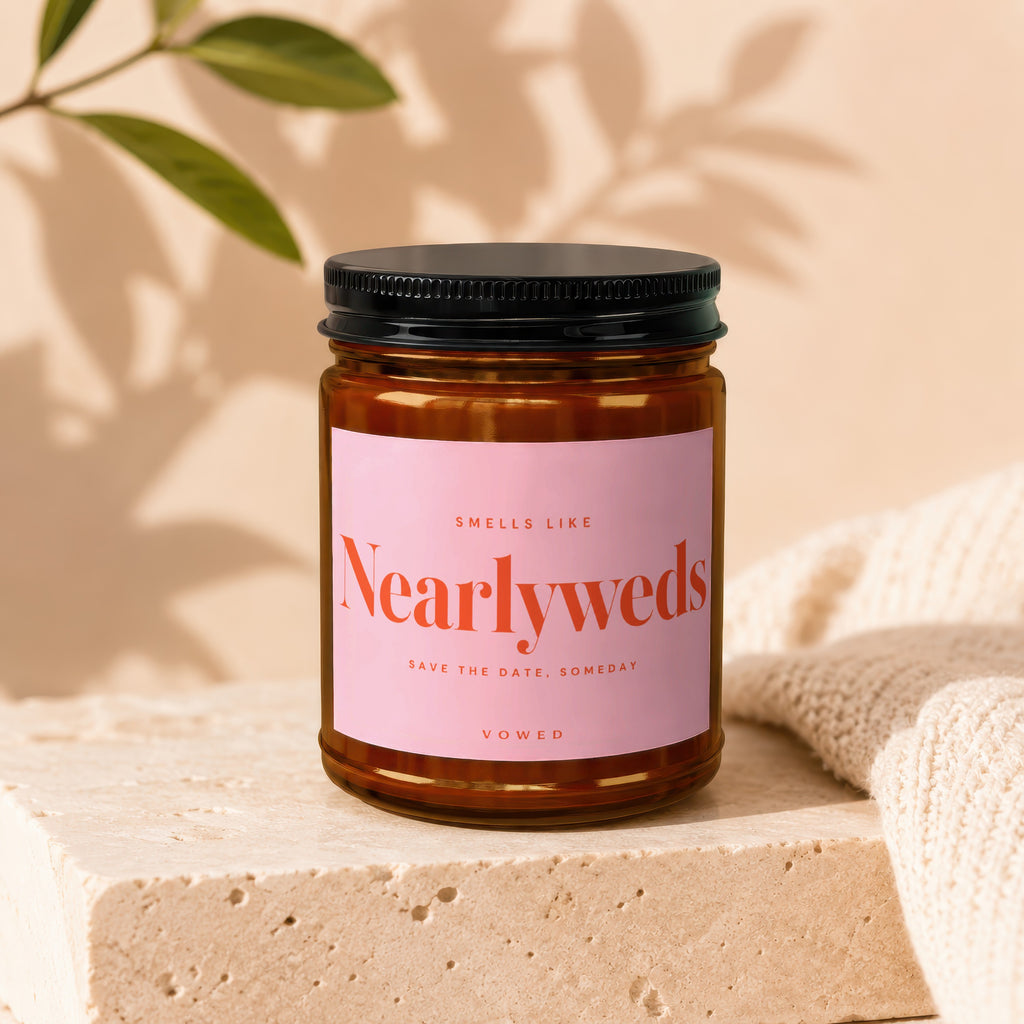 Amber jar candle with pink label reading "Smells Like Newlyweds Save the Date, Someday Vowed".