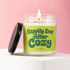 Glass candle with a lit wick and lid. Label says "Happily Ever After Cozy Vowed".