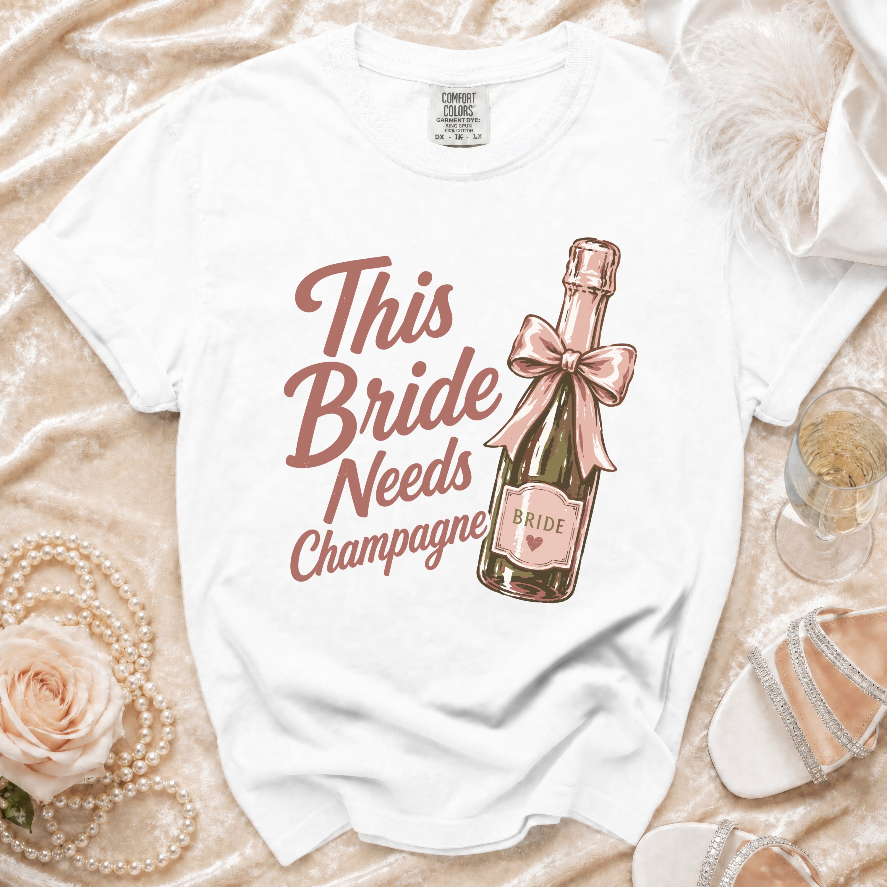 White t-shirt with "This Bride Needs Champagne" text and champagne bottle graphic.