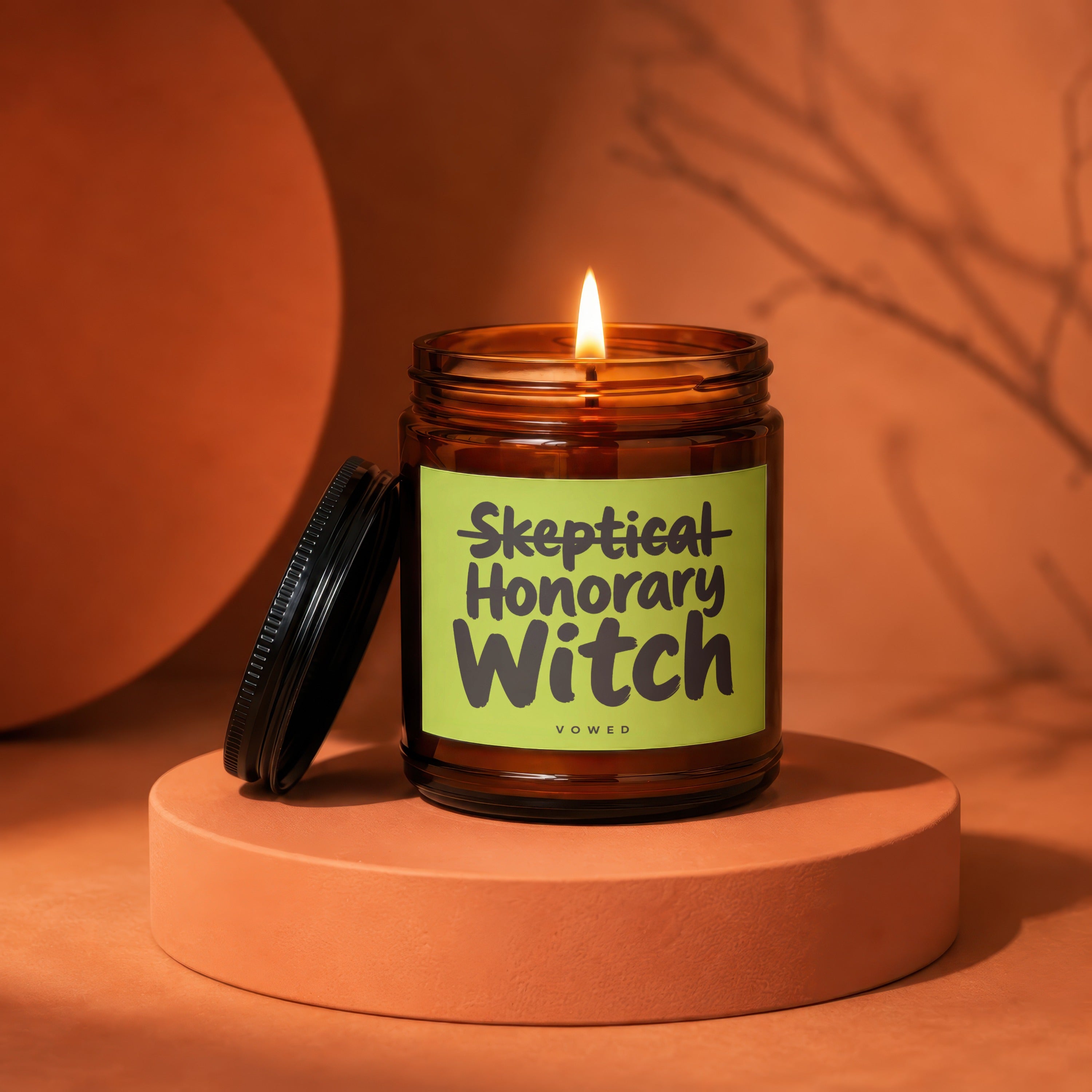 Burning amber glass candle with "Skeptical Honorary Witch" printed on its label.