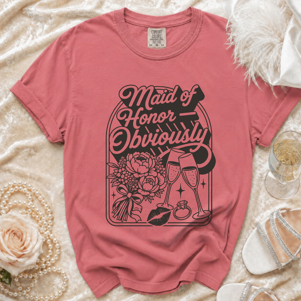Pink t-shirt with "Maid of Honor Obviously" graphic, champagne flutes, flowers, lips, and ring.