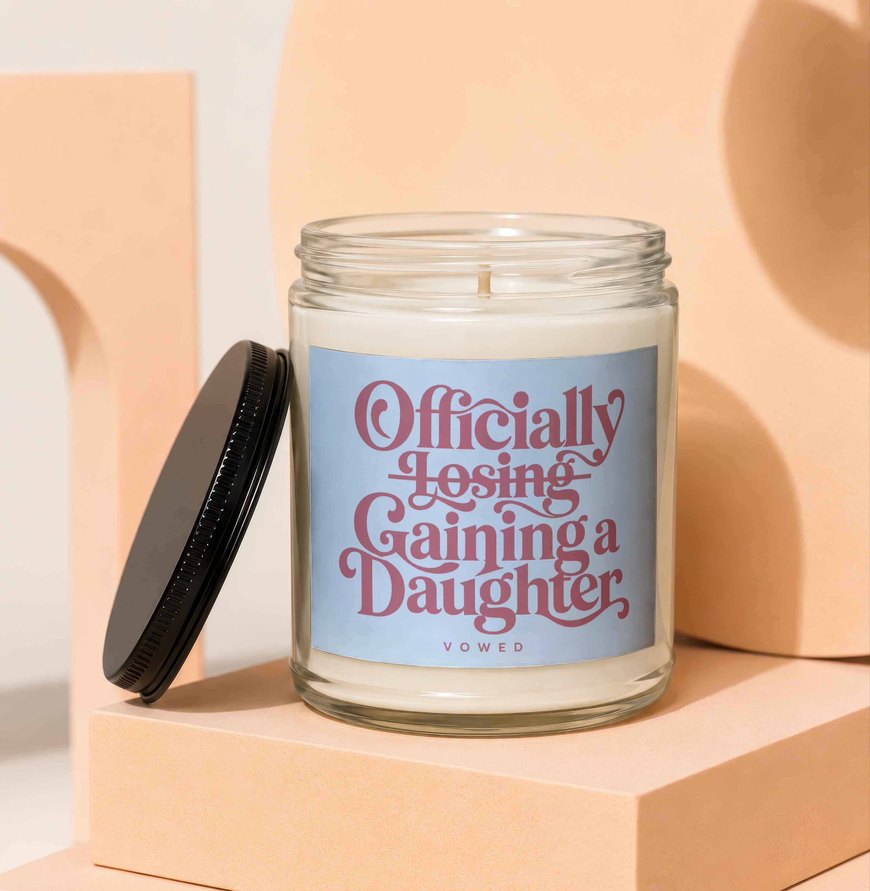Glass candle with light blue label reading "Officially Losing, Gaining a Daughter".