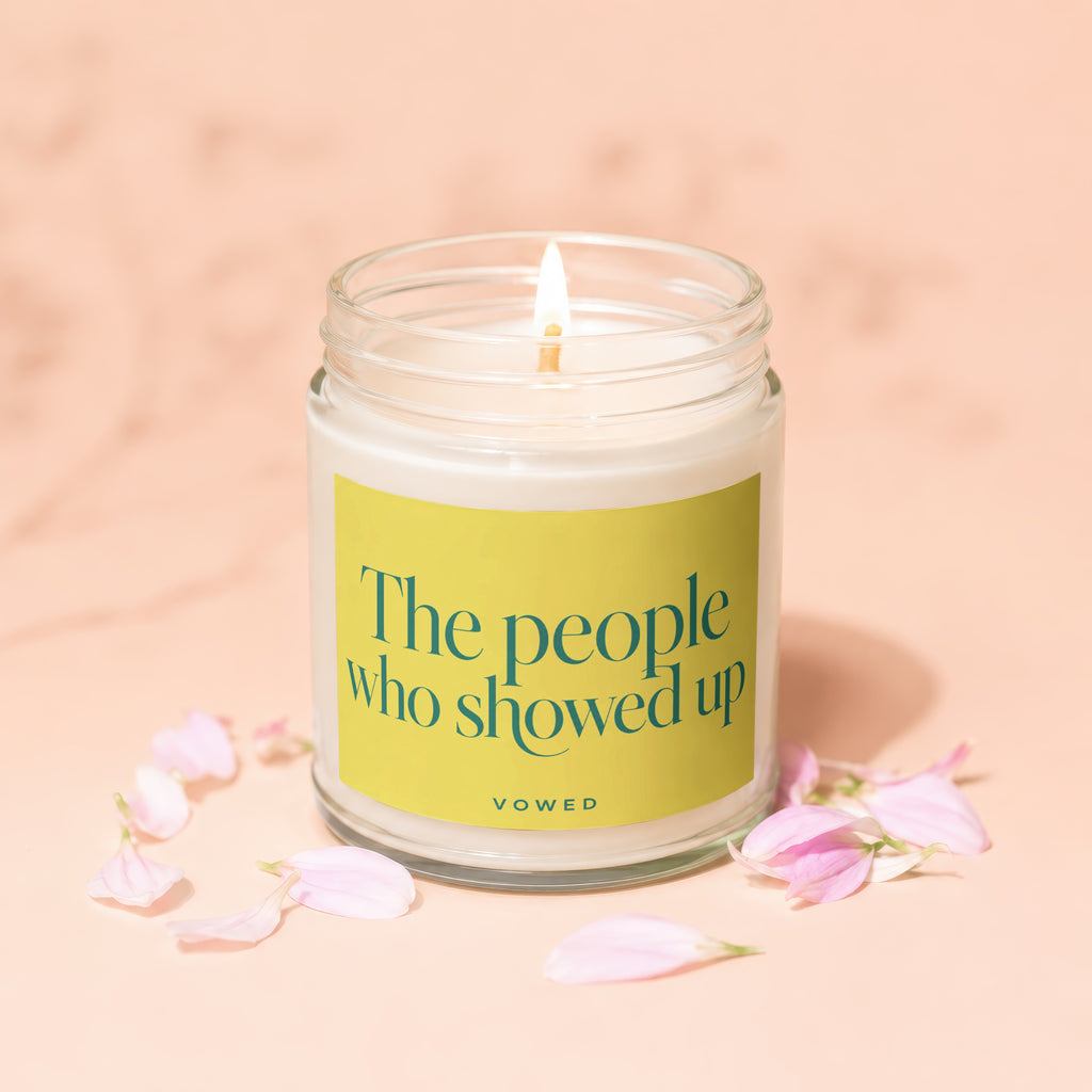 Lit candle in a glass jar with yellow label text "The people who showed up VOWED".