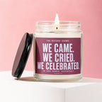 Lit candle in a glass jar with a maroon label reading "We Came. We Cried. We Celebrated."