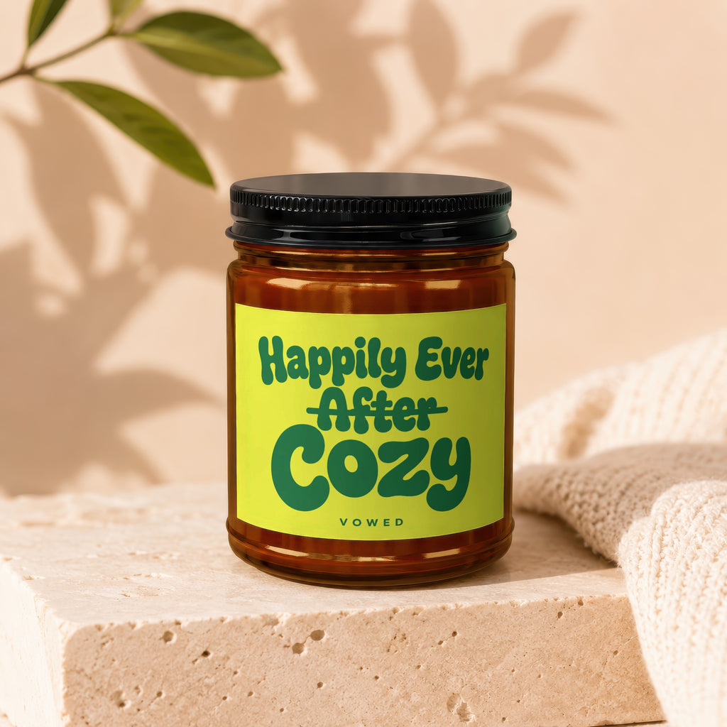 Candle labeled "Happily Ever After Cozy" on a stone block with knitted fabric.