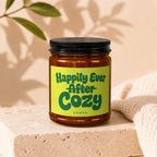 Candle labeled "Happily Ever After Cozy" on a stone block with knitted fabric.