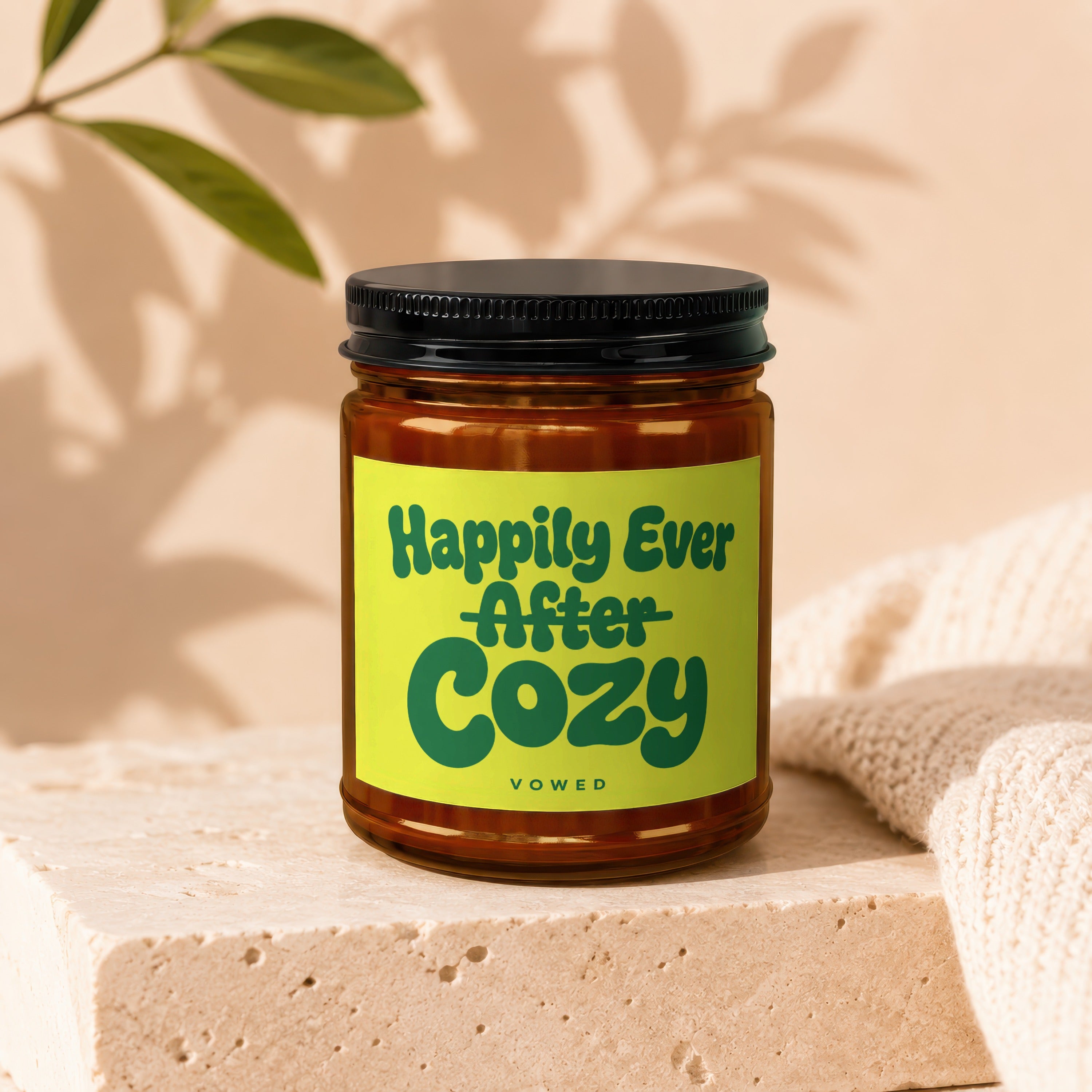 Candle labeled "Happily Ever After Cozy" on a stone block with knitted fabric.