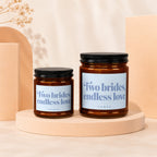 Two amber glass candles with black lids, labeled "Two brides, endless love."
