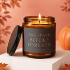 Amber jar candle with lit flame, "The Spark Before Forever" text, and autumn decor.