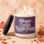 Glass candle with flickering flame on purple label reading "Blessed Cursed Together Forever Vowed."